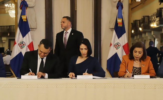 Funcionarios firmando acuerdo oficial con banderas dominicanas