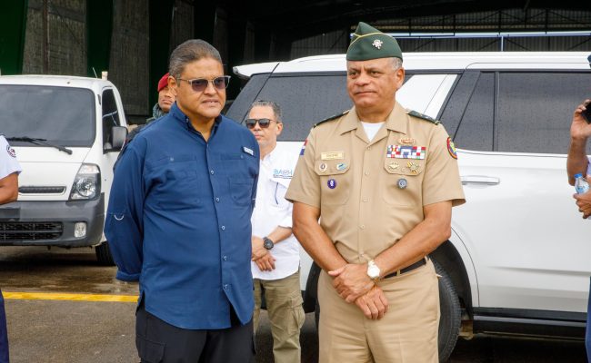 Funcionarios junto a militar frente a vehículos oficiales