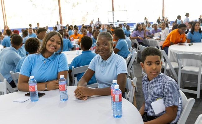 Estudiantes en evento escolar sentados en mesas