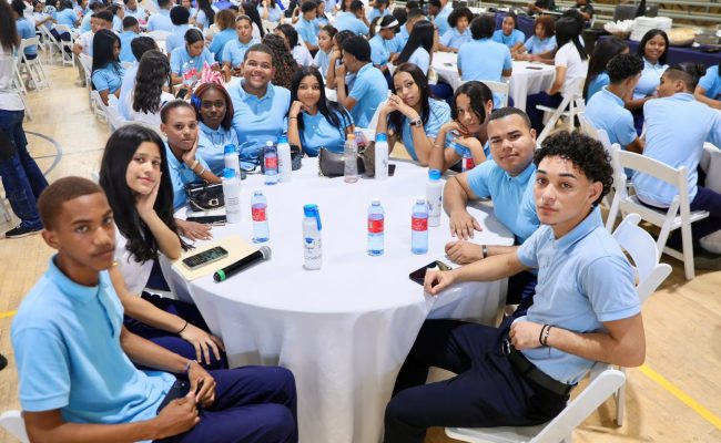 Estudiantes en evento escolar sentados en mesa redonda